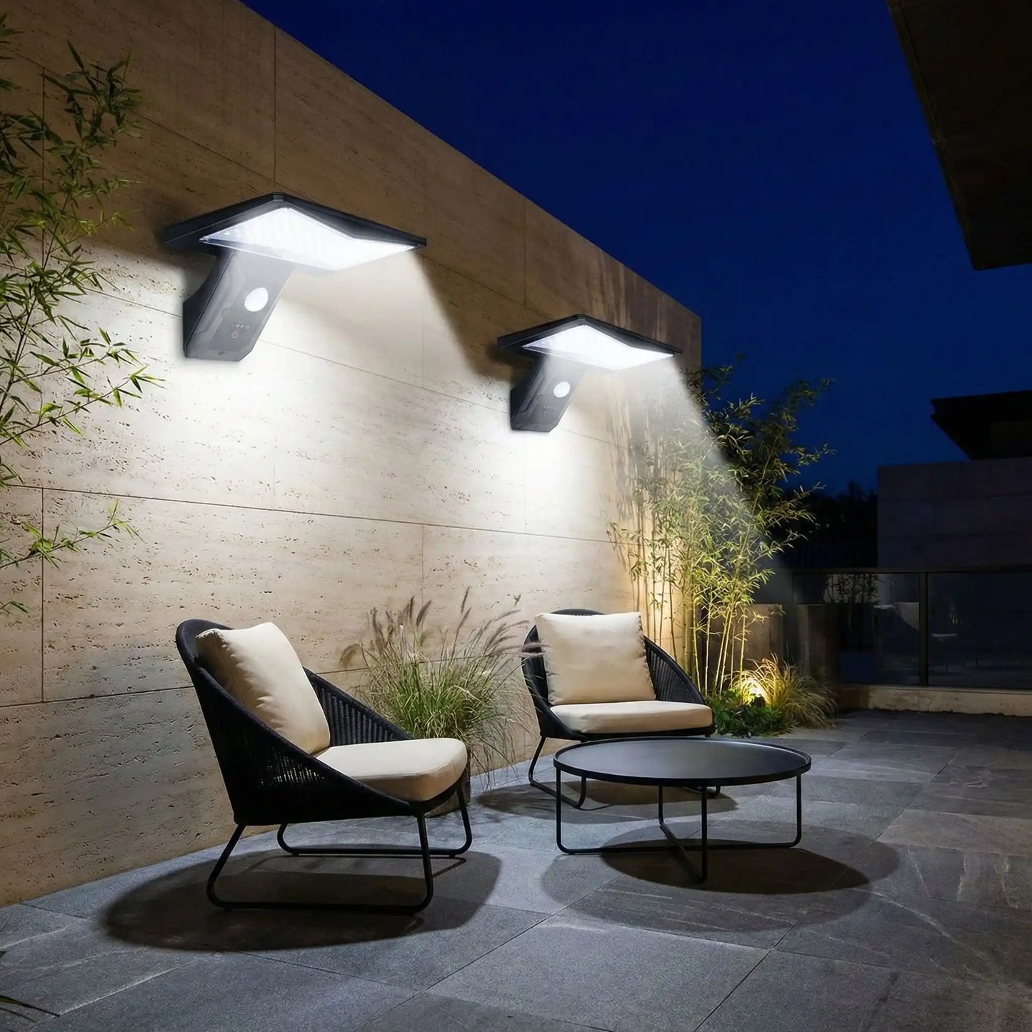 applique extérieure avec détecteur sur mur dans jardin éclairant deux fauteuils et une table basse la nuit et bambous