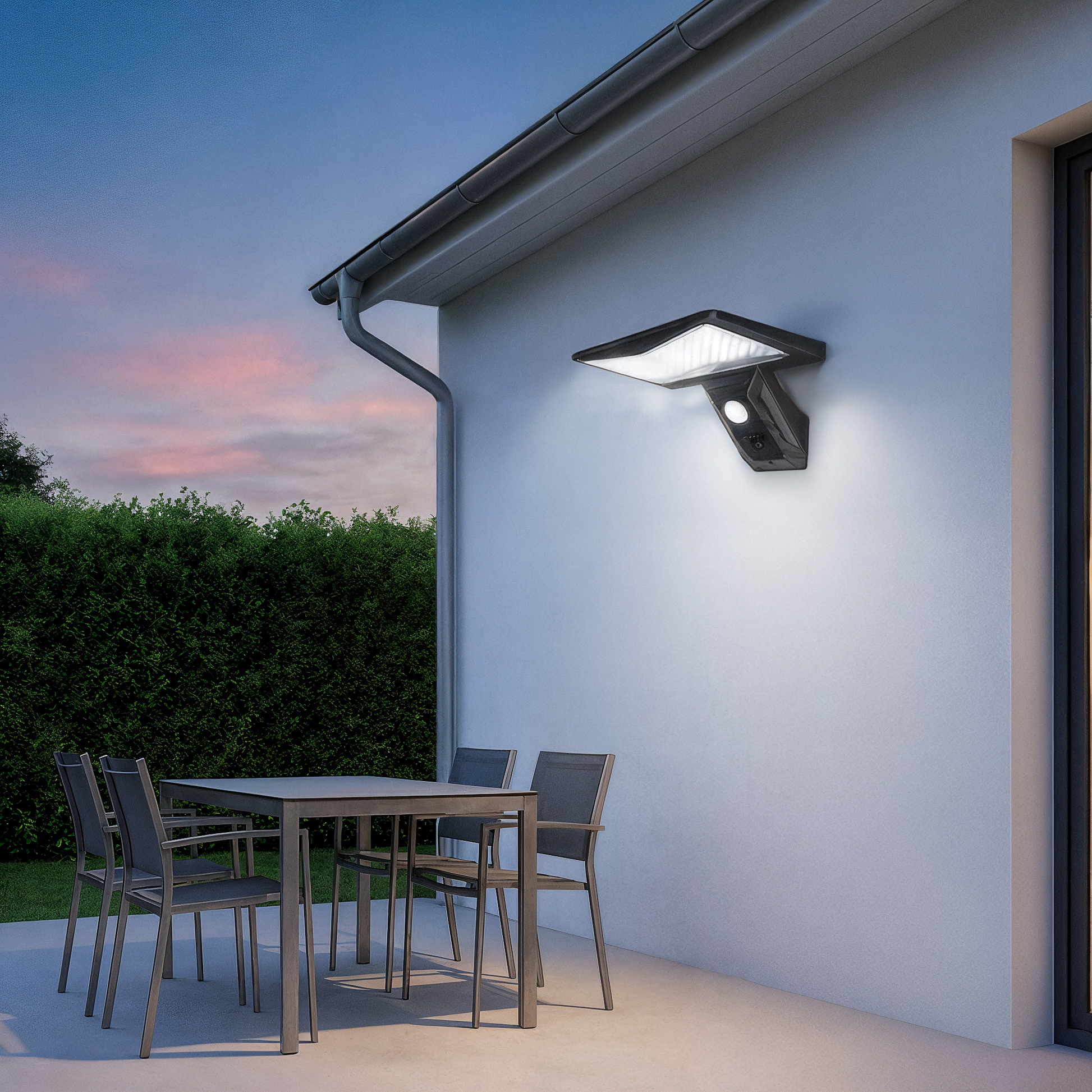 applique extérieure avec détecteur sur mur extérieur d'une maison moderne. Terrasse avec table et 4 chaises et haie verte et pelouse