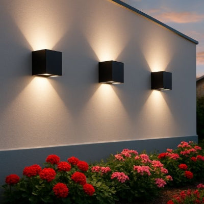 Applique murale extérieur noire illuminant un mur blanc avec massif fleuri.