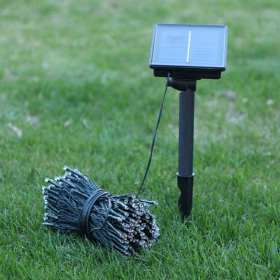 Guirlande exterieur solaire enroulée sur le sol dans l'herbe avec le capteur solaire au plein jour