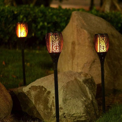 Lampe solaire extérieur effet flamme disposée près de rochers pour illuminer le jardin de nuit.