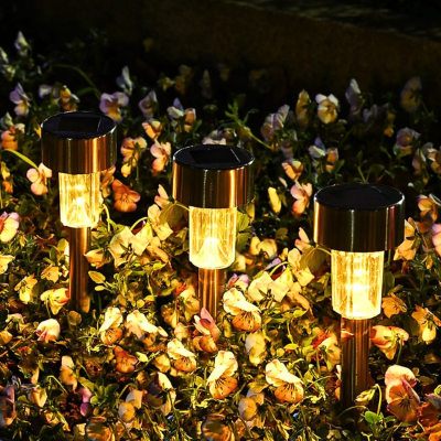 Lampe solaire extérieur LED éclairant un massif de fleurs colorées au crépuscule.