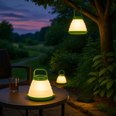 lanterne exterieur une accrochée à un arbre et deux autres posées au sol et sur une table basse. Joli jardin vert au crépuscule