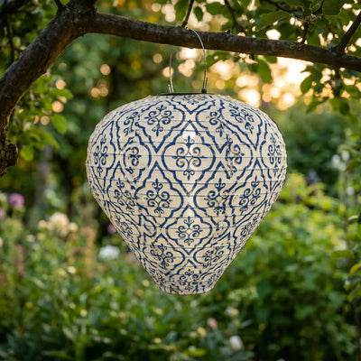 lanterne solaire jardin Zorah, tissu blanc à motifs arabesques bleus, suspendue à une branche au crépuscule