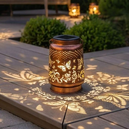 Lanternes solaires avec motifs papillons projetés sur terrasse extérieure créant une ambiance chaleureuse en lumière blanc chaud